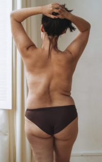 Self loving attractive woman plus size in underwear from back near window at light room, body love